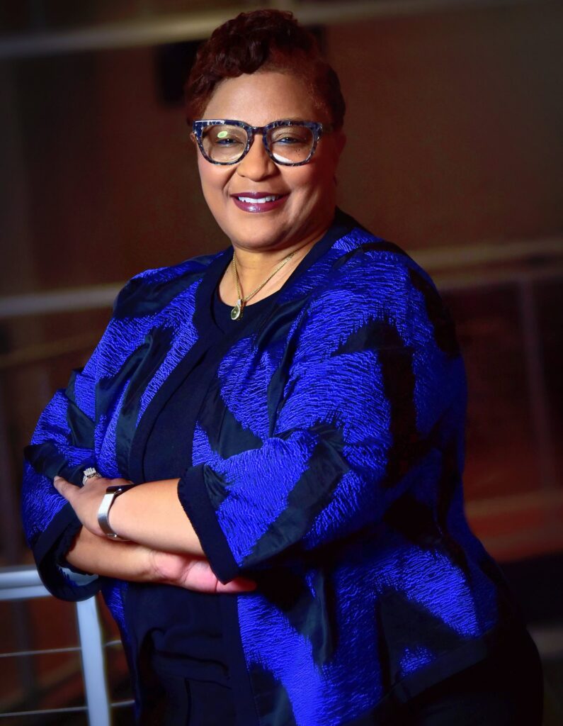 Commissioner Carmen Moore-Zeigler in a royal blue jacket, arms crossed, smiling